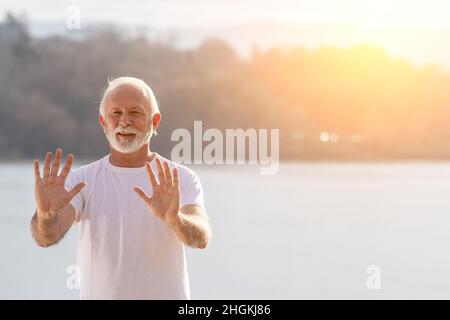 Ritratto di uomo anziano praticando tai chi chuan all'aperto al tramonto sulla costa del fiume Foto Stock