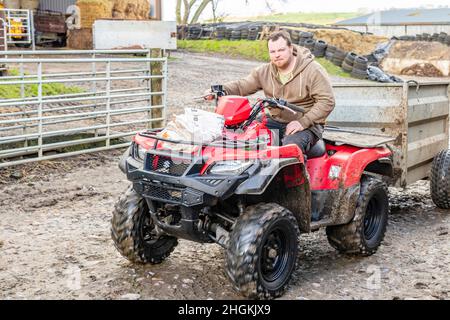 Giovane agricoltore maschio che guida quad rosso in fattoria Matfen Northumberland Foto Stock