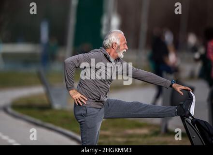 Uomo anziano in tuta che si allunga dopo l'allenamento in palestra pubblica Foto Stock