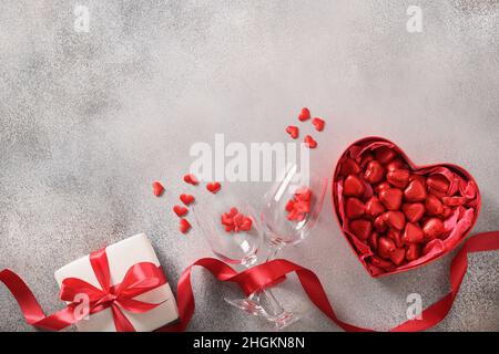 Carta romantica di San Valentino con vino rosso, regalo e rose rosse su sfondo grigio. Vista dall'alto. Spazio di copia. Foto Stock