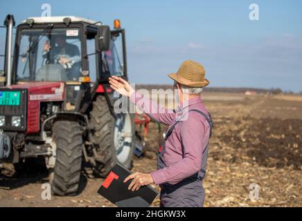 Agricoltore maturo che guida il trattore e parla con un uomo anziano sul campo Foto Stock