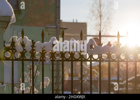 Recinzione in città in inverno primo piano. Il sole basso illumina la recinzione in ferro battuto innevata. Foto Stock