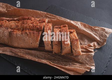 baguette di cereali tagliata a pezzi su carta pergamena su sfondo nero Foto Stock