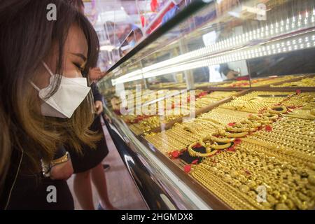 Bangkok, Thailand. 21st Jan, 2022. A customer wearing a face mask as a protective measure against the spread of Covid-19 looks on at the display of gold jewelry at a gold shop in Bangkok's Chinatown.Gold shops in Bangkok's china town prepare for business before the upcoming Chinese New Year 2022 in Thailand. (Photo by Adisorn Chabsungnoen/SOPA Imag/Sipa USA) Credit: Sipa USA/Alamy Live News Stock Photo