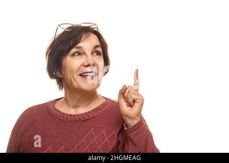 Ritratto di attraente allegro intelligente matura donna puntando a forefinger isolato su sfondo bianco colore. Foto Stock