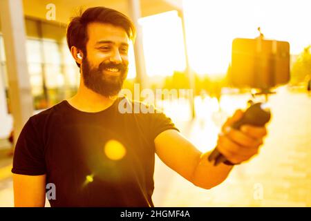 uomo bearded in cotone nero t-shirt registrazione video per vegan blog all'aperto nel parco estivo al tramonto luce oro Foto Stock