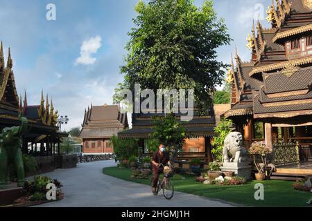 A Wat Sanghathan, un famoso tempio di meditazione a Nonthaburi, in Thailandia, un ciclista passa davanti a uno dei padiglioni ornati in legno del tempio. Foto Stock