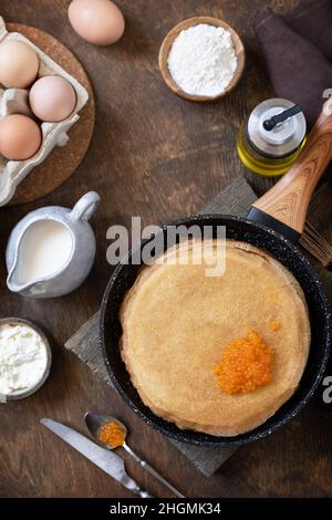 Frittelle di cucina tradizionale russa. Pancake sottili serviti con caviale rosso su un tavolo di legno. Vista dall'alto sfondo piatto. Foto Stock