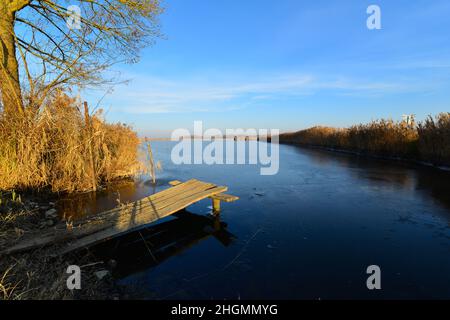 Un grande laghetto con un piccolo molo in una fredda giornata di sole a fine autunno. Foto Stock