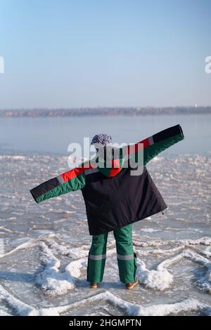 Una donna in un colorato costume termale che gode l'inverno mentre si erge su un lago ghiacciato con cielo blu sullo sfondo. Libertà Foto Stock