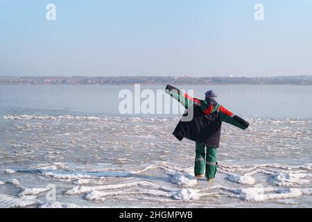 Una donna in un colorato costume termale che gode l'inverno mentre si erge su un lago ghiacciato con cielo blu sullo sfondo. Libertà Foto Stock
