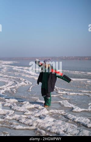 Una donna in un colorato costume termale che gode l'inverno mentre si erge su un lago ghiacciato con cielo blu sullo sfondo. Libertà Foto Stock