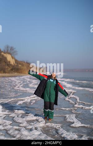 Una donna in un colorato costume termale che gode l'inverno mentre si erge su un lago ghiacciato con cielo blu sullo sfondo. Libertà Foto Stock