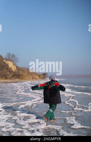 Una donna in un colorato costume termale che gode l'inverno mentre si erge su un lago ghiacciato con cielo blu sullo sfondo. Libertà Foto Stock