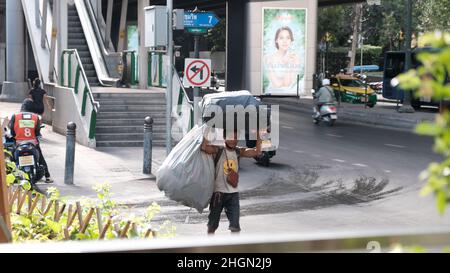 Classe di lavoro Eroe maschio pedonale Passeggiate trasporto sacchetti di plastica Trash su Sukhumvit Road Bangkok Thailandia Foto Stock