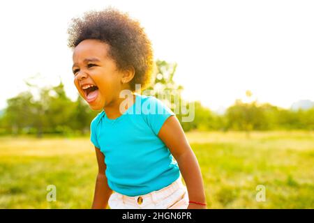 adorabile piccola ragazza di razza mista che cammina da sola nel parco al tramonto Foto Stock