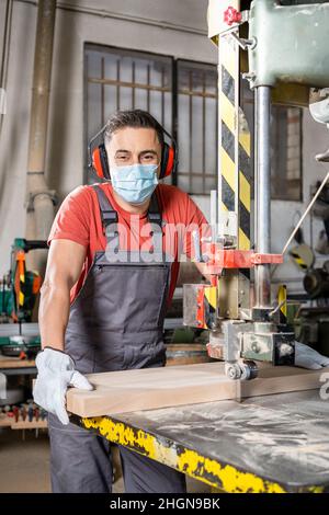 Operatore in maschera taglio asse su sega a nastro Foto Stock