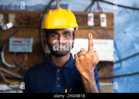 Concentratevi sul posto di lavoro, ingegnere elettrico con elmetto sul posto di lavoro che mostra il dito d'inchiostro votato guardando la fotocamera - concetto di elezioni indiane, democrazia Foto Stock