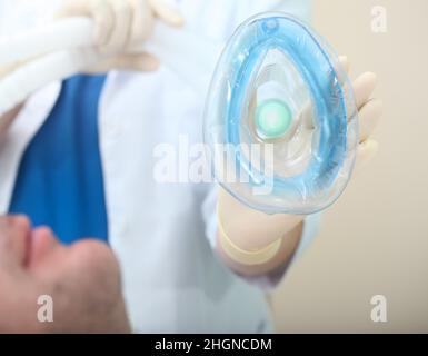 Paziente maschio prima dell'anestesia respiratoria con maschera respiratoria nelle mani del medico femminile. Foto Stock