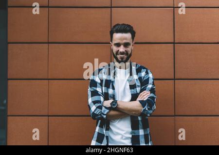 Ritratto di mezza lunghezza di turista allegro maschio con le mani incrociate che sorridono alla macchina fotografica durante il tempo di viaggio Foto Stock