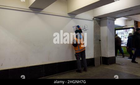 Rimozione dei graffiti dai vandali nel passaggio sotterraneo. Dipendente della città, indossando una uniforme arancione, pulisce le pareti dai graffiti e dalla scrittura, con un rosso Foto Stock