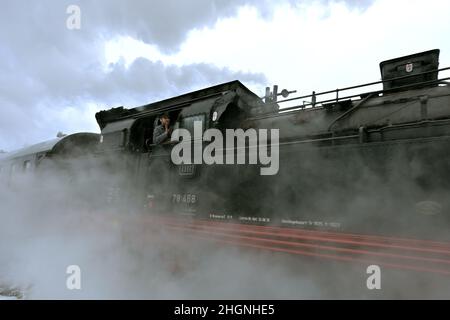 Winterberg, Germania. 22nd Jan 2022. L'ingegnere ondeggia mentre il treno storico passa attraverso la città innevata nella regione di Sauerland. La storica locomotiva a vapore è un T18 prussiano del 1920s. Con il titolo "Rodeldampf ins Sauerland", la Bielefeld Railway Friends Association guida una storica locomotiva a vapore da Bielefeld a Winterberg. A bordo ci sono diverse centinaia di fan della ferrovia, che slittano sulle piste con le loro slitte a destinazione. Il treno si ferma anche a Paderborn, Lippstadt, Soest, Unna e Arnsberg, tra gli altri luoghi. Credit: David Inderlied/dpa/Alamy Live News Foto Stock