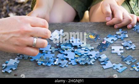 Una mano che arriva per un pezzo di un puzzle sparso su un pavimento di legno Foto Stock