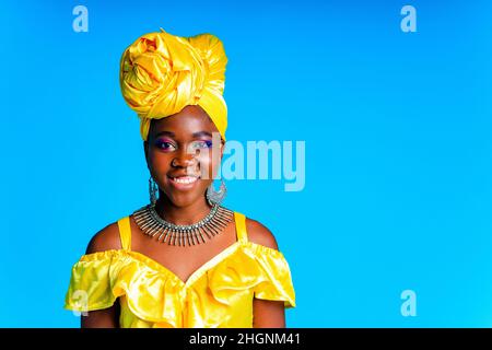 Donna africana con turbante di seta gialla e orecchini in argento e piercing al naso in blu studio sfondo Foto Stock