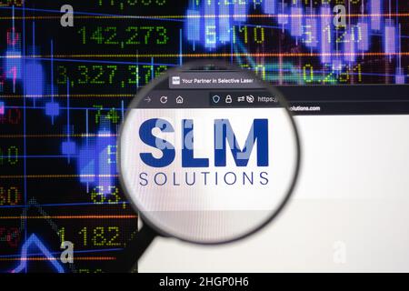 SLM Solutions logo azienda su un sito web con blurry sviluppi del mercato azionario in background, visto su uno schermo del computer attraverso una lente d'ingrandimento. Foto Stock