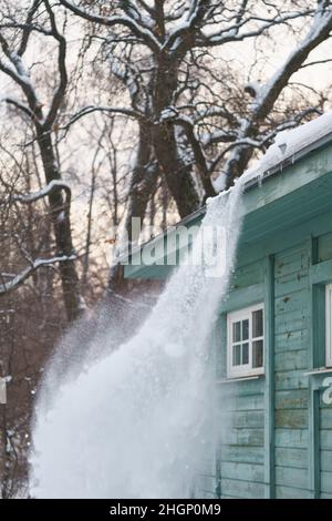 Processo di pulizia del tetto dalla neve con la pala. Pericolo di caduta di neve o ghiaccioli dal tetto Foto Stock