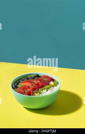 ciotola per frullati con frutti e bacche fresche in un piatto blu con ombra gialla scura Foto Stock