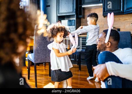 famiglia ispanica multiculturale che indossa le orecchie di coniglio in soggiorno luce soft sole giorno Foto Stock