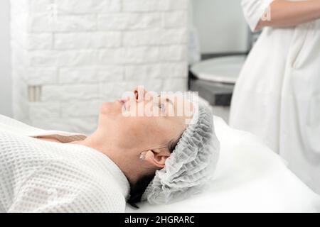 Donna matura che riceve maschera per il trattamento del viso nel salone di bellezza termale. Concetto di cura della pelle per le persone anziane Foto Stock