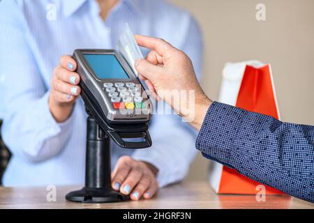 Un uomo effettua acquisti online utilizzando un terminale mobile. Passa una scheda di plastica attraverso il lettore di terminali Foto Stock