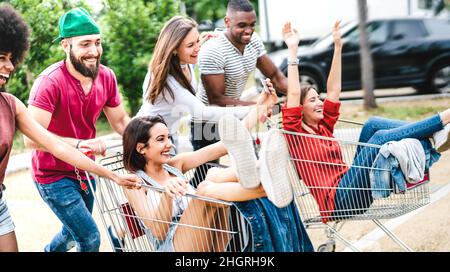 Felici persone multiculturali divertirsi insieme sul carrello - amici Milenial condividere il tempo con i carrelli al parcheggio del centro commerciale Foto Stock