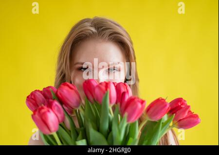 Donna con un bouquet di tulipani rossi su sfondo giallo. La ragazza felice in un vestito nero tiene un'armatura di fiori . Regalo per San Valentino. La maggior parte Foto Stock