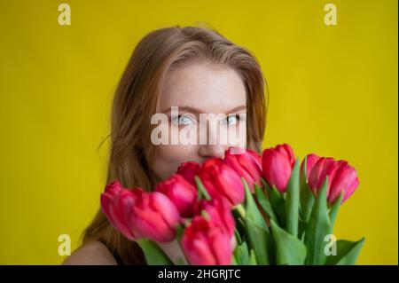 Donna con un bouquet di tulipani rossi su sfondo giallo. La ragazza felice in un vestito nero tiene un'armatura di fiori . Regalo per San Valentino. La maggior parte Foto Stock