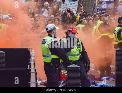 Londra, Regno Unito 22nd gennaio 2022. Gli ufficiali della polizia si trovano fuori Downing Street, circondati dal fumo di un fiaccato lanciato da un manifestante. Migliaia di persone hanno marciato attraverso il centro di Londra per protestare contro i vaccini obbligatori per lo staff NHS, maschere facciali, vaccini covidi, passaporti di vaccinazione e varie altre rimostranze alimentate da teorie di cospirazione. Credit: Vuk Valcic / Alamy Live News Foto Stock