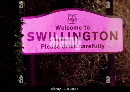 Un cartello nel villaggio di Swillington che accoglie i conducenti attenti è illuminato dai segnalatori luminosi della polizia dopo un incidente stradale su Aberford Road. Foto Stock