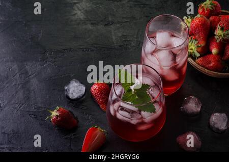 Cocktail estivo freddo con ghiaccio in bicchieri e fragole. Vista dall'alto, in una vena scura. Foto Stock