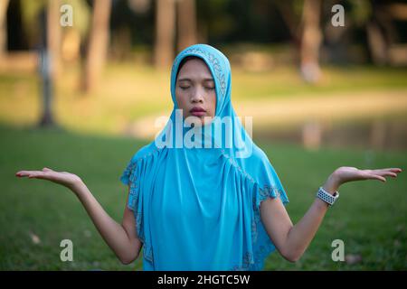 Bella ragazza musulmana che si rilassa nel parco della città con yoga antistress formazione Foto Stock