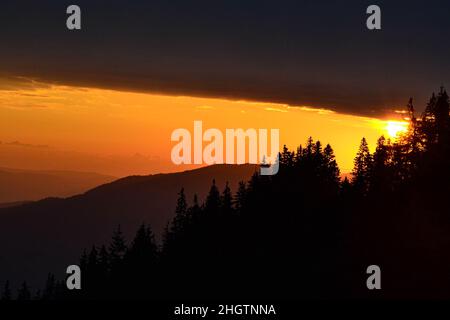 Colorito sorgere del sole sulle montagne viste dall'alta quota. Vista panoramica delle montagne di silhouette contro il cielo arancione Foto Stock