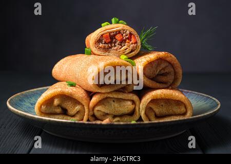 Le frittelle fritte farcite di carne e carote sono decorate con cipolle fresche e aneto su sfondo scuro da vicino. Vista laterale. Foto Stock