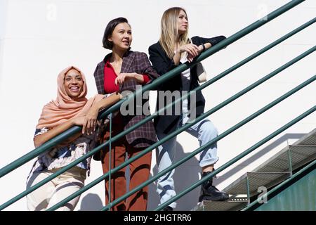 Soddisfare giovani donne diverse guardare lontano mentre si piedi sulle scale in città Foto Stock