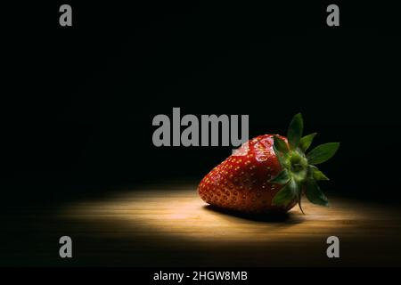 Una fragola su un terreno in legno ad alto contrasto. Foto Stock