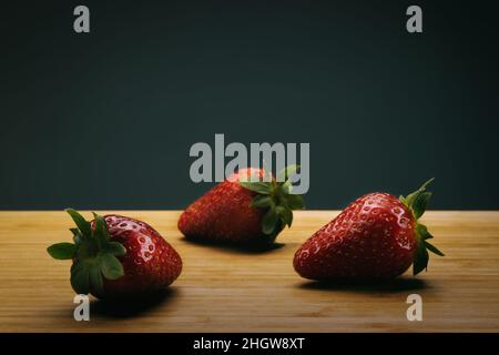 Tre fragole su un terreno di legno immagine ad alto contrasto. Foto Stock