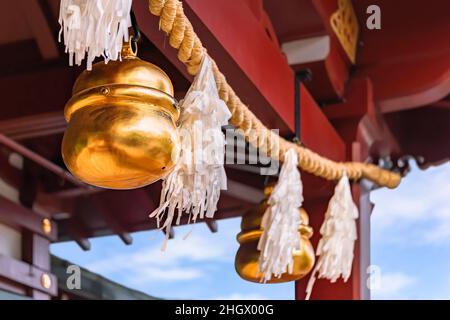 Lucenti campane di suzu dorate appese su una corda di paglia di grano o di riso shimenawa adornata da streamers sospesi noti come shide e realizzati con lavi giapponesi Foto Stock