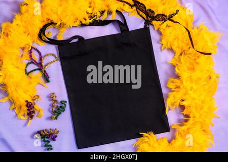 Borsa tote Mardi Gras Mockup nera con maschera carnevale e boa di piume giallo Foto Stock