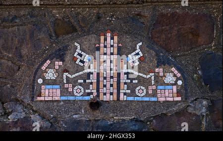 Un bellissimo mosaico rosa, blu, bianco e nero. Le piastrelle sono su un muro di pietra e molto vecchie. Foto Stock