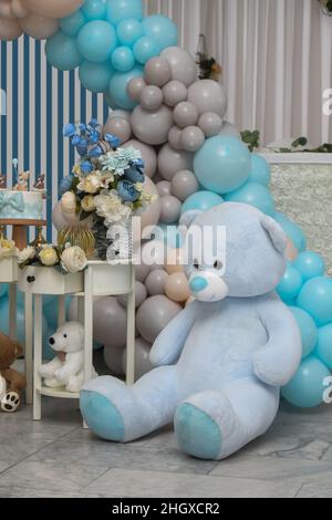 Orsacchiotto siede sullo sfondo con diversi colori di palloncini, ghirlanda di compleanno, fiori blu e bianchi. Festeggiamo il primo anno di vita del bambino. Decorare Foto Stock